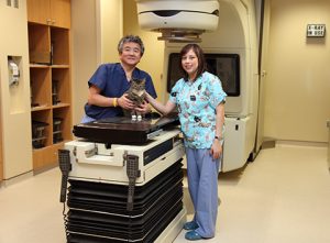 Two oncologists standing with a radiation machine and a cat 