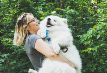 A woman smiles while carrying a happy dog