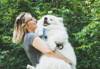 A woman smiles while carrying a happy dog