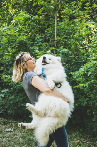 A woman smiles while carrying a happy dog