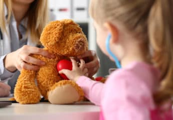 Child using toy stethoscope with teddy bear