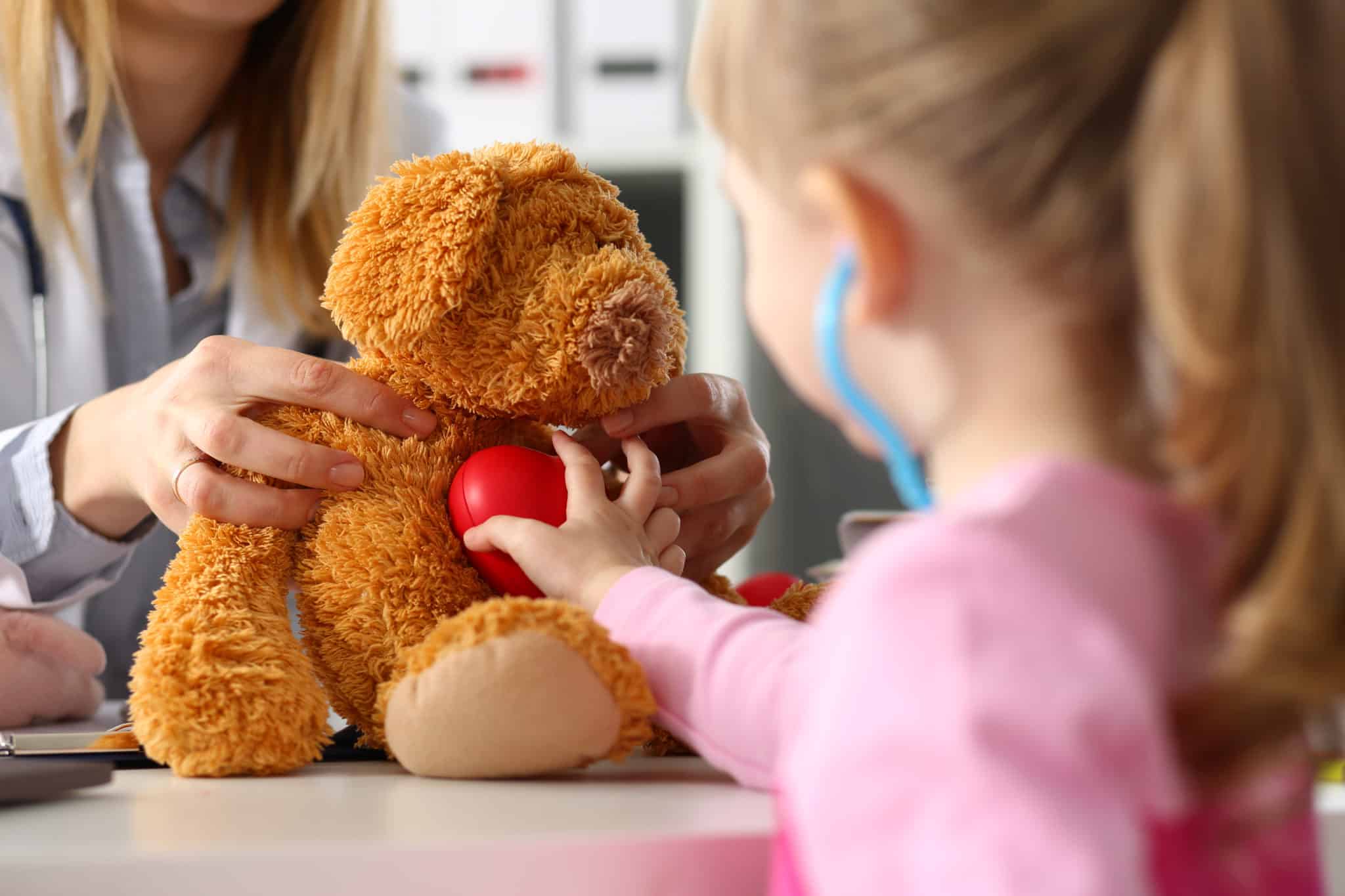 Child using toy stethoscope with teddy bear